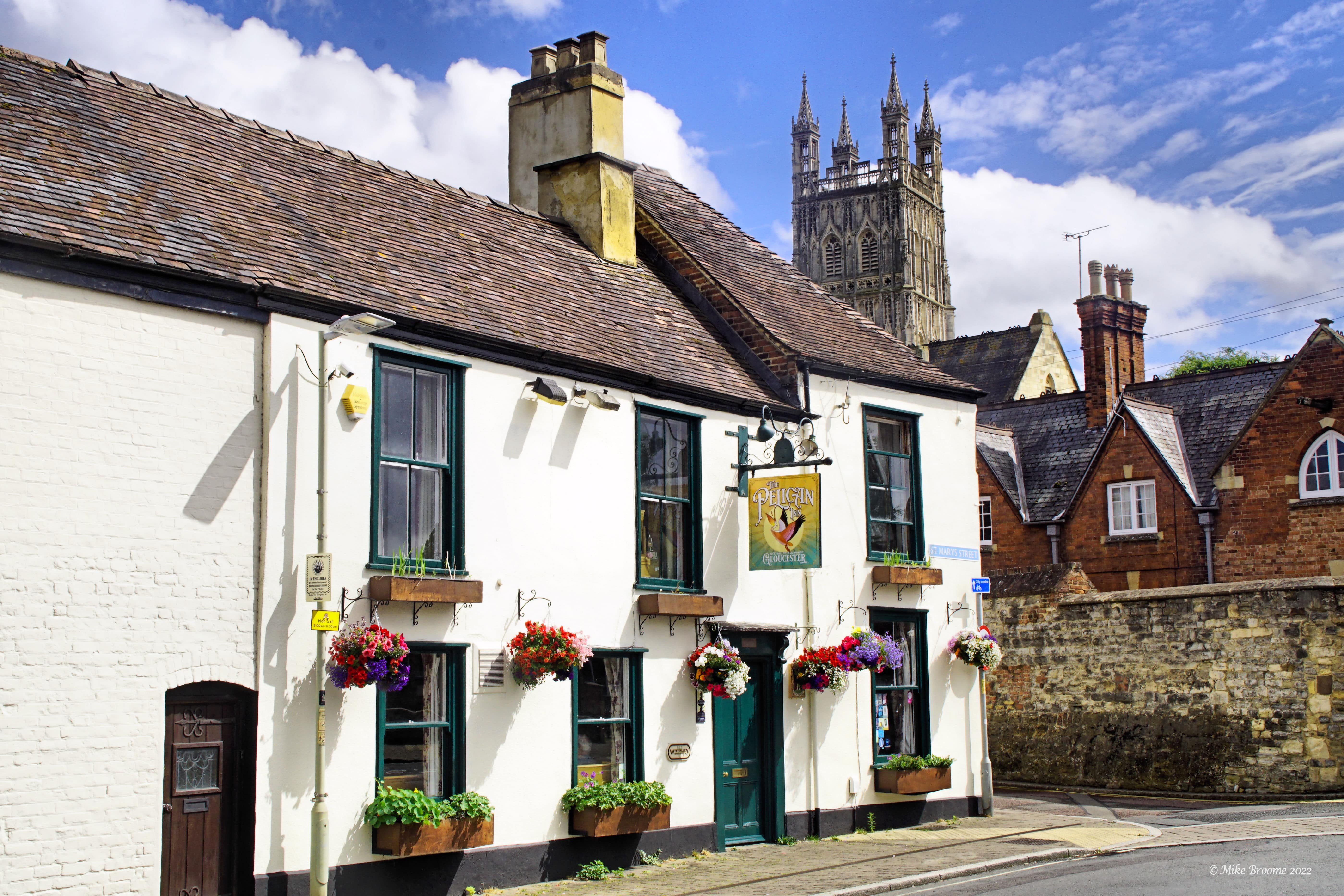 A white pub with green window frames and plant window boxes. The background there is a large cathedral