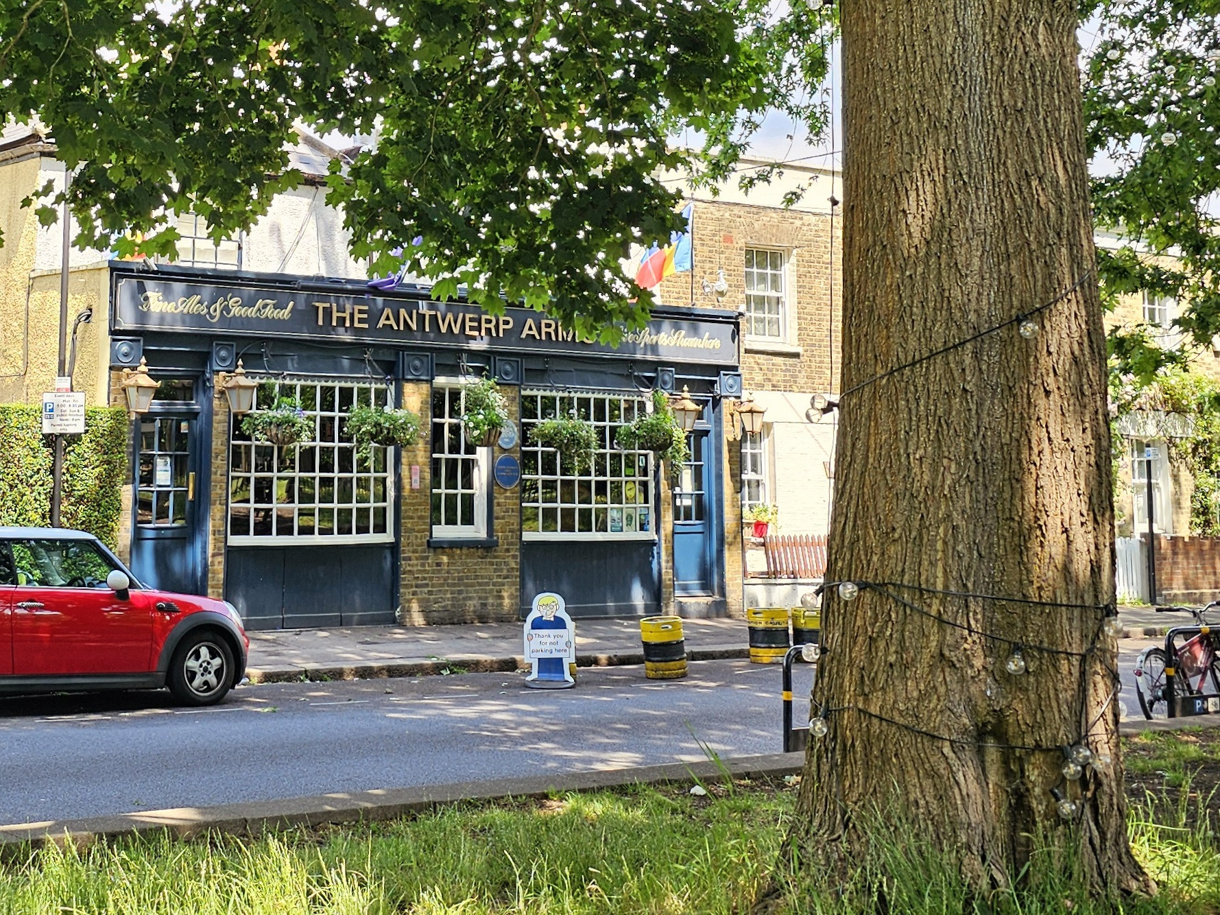 A blue pub is in the background with a red mini cooper to the left. on the right, in the foreground is a tree truck.