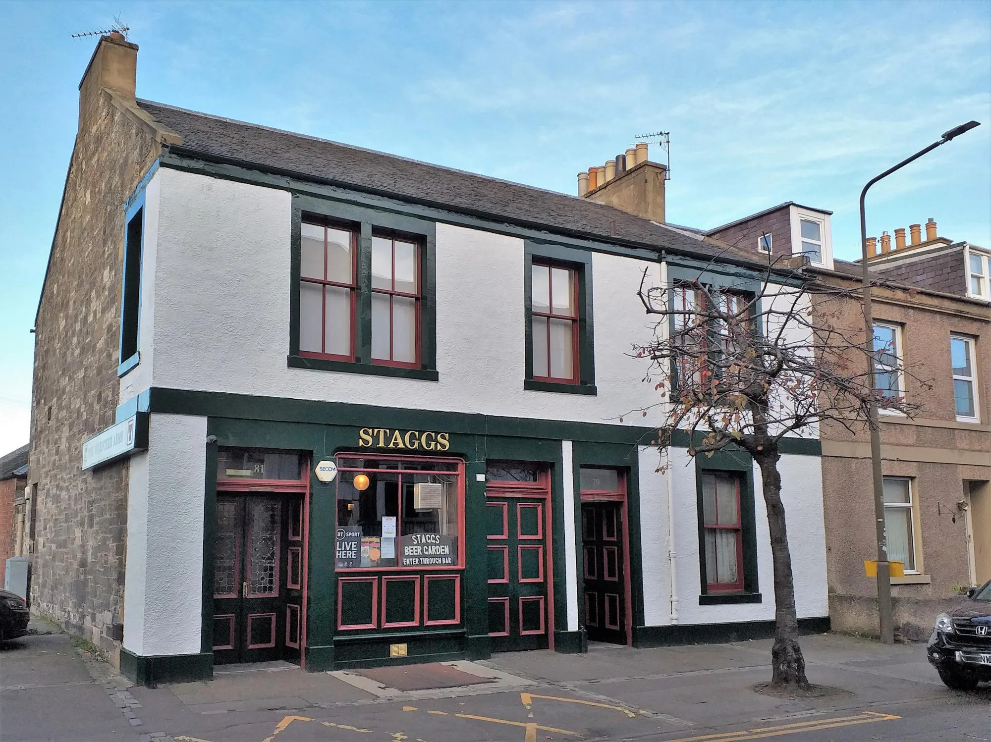 A white pub with dark green and ref window and door frames. There is a tree and a lamppost to the right of the pub