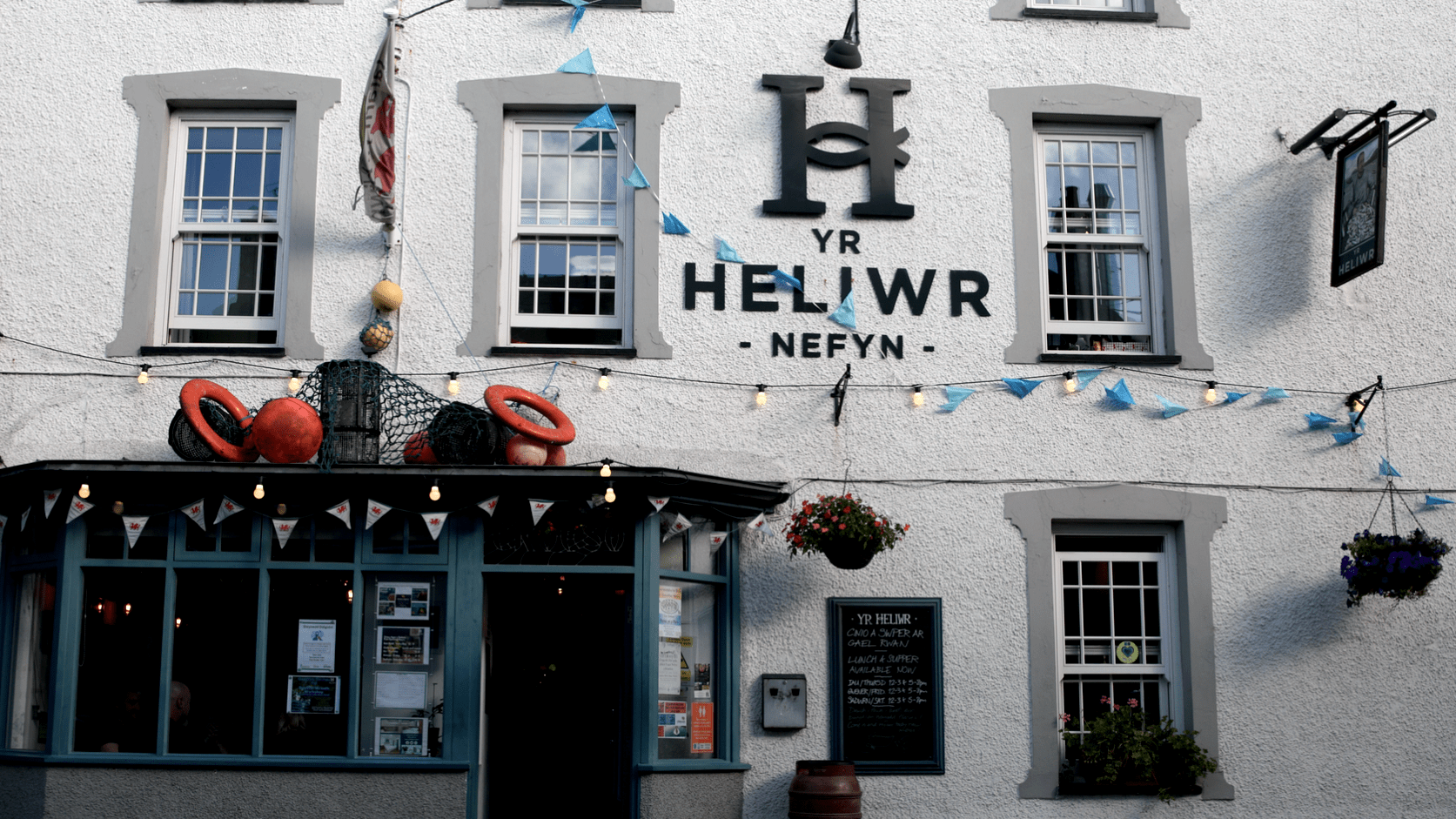 A white building with a large letter H in the centre between windows. In the bottom left corner is a grey entrance