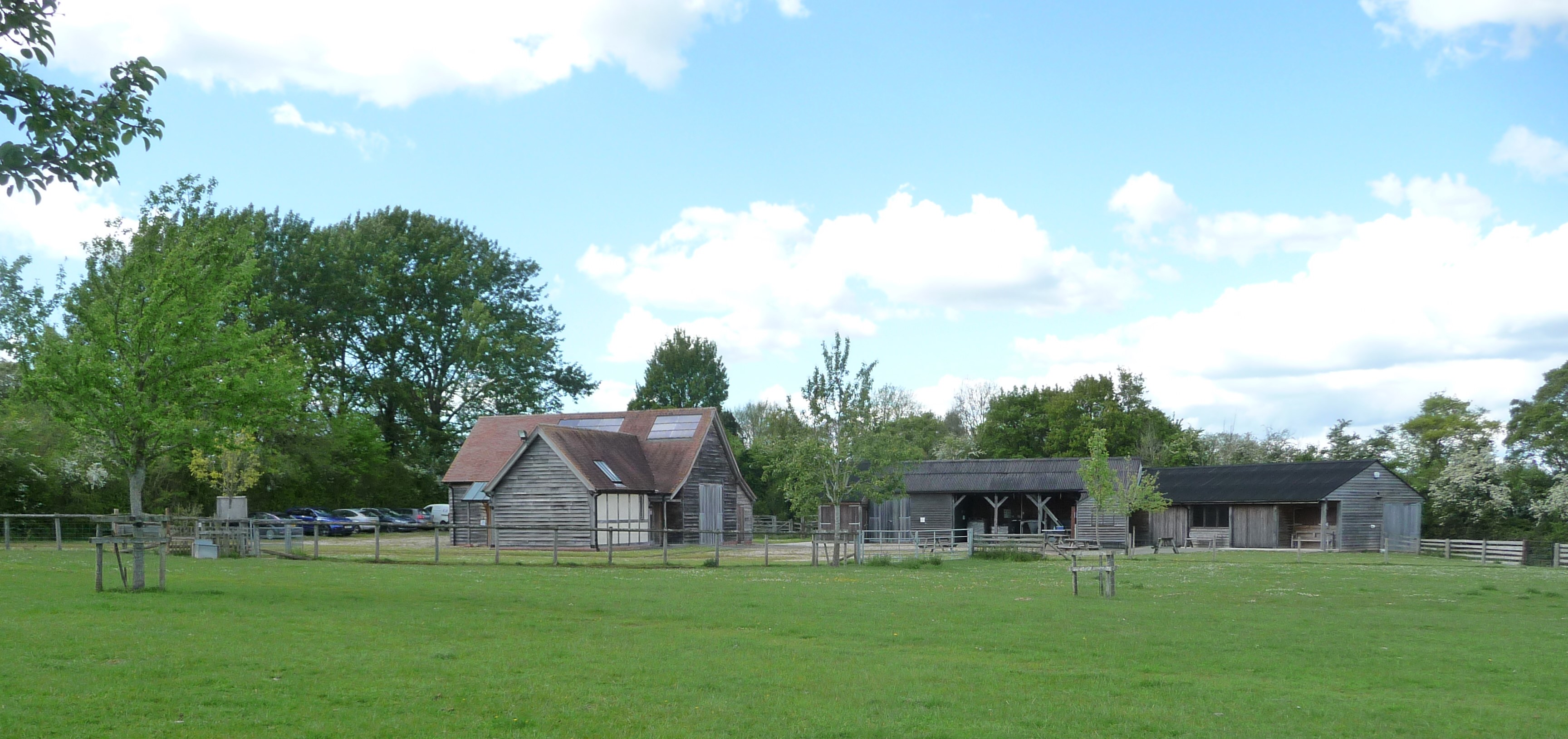 A series of wooden barns in a lrge grassy field. There are trees around and behind the buildings